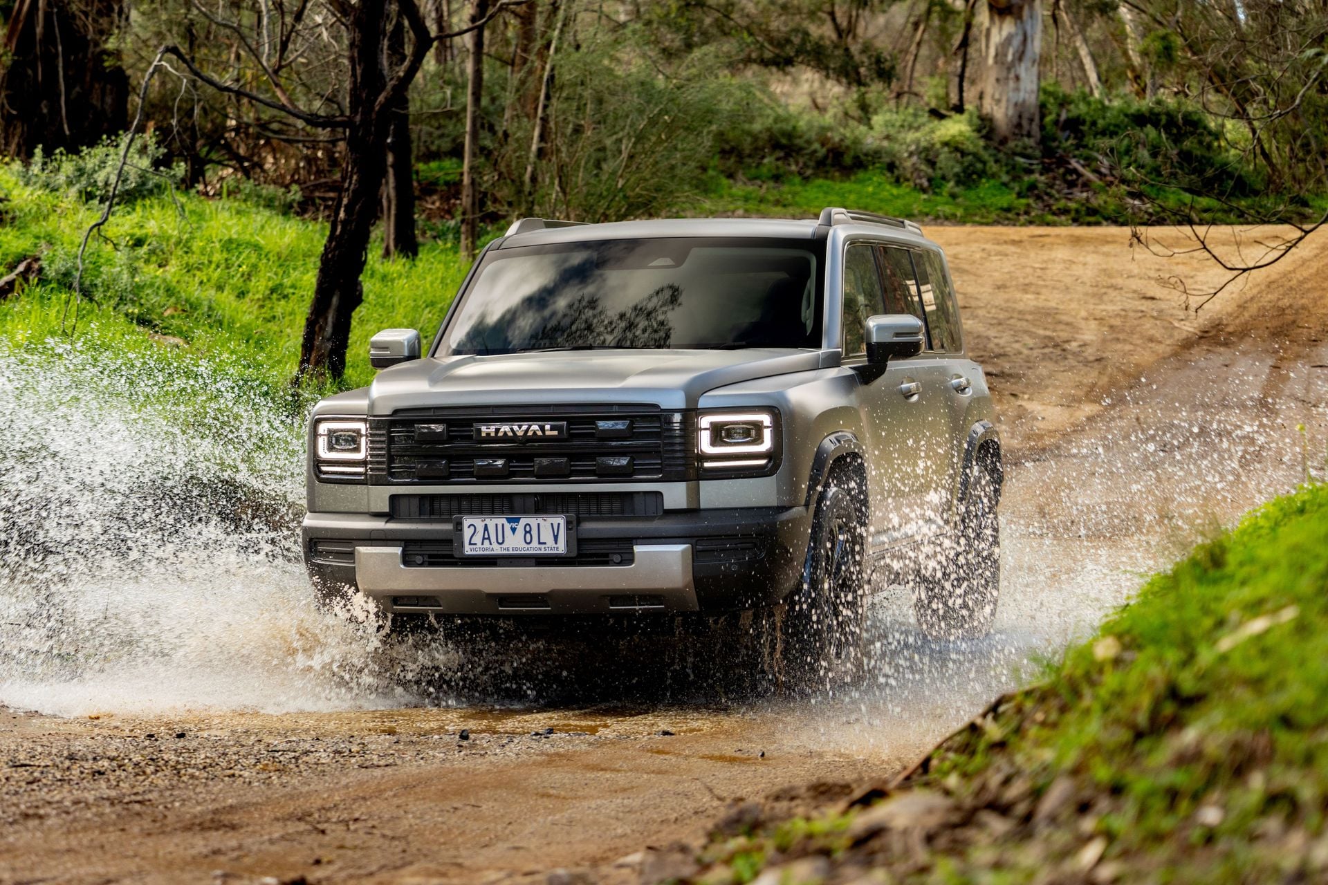 A grey Haval H7 SUV seen from the front while driving through a water crossing on an off-road track surrounded by bushland