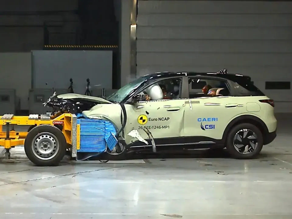 A light green SUV undergoes a Euro NCAP frontal offset crash test, with the front end heavily damaged and airbags deployed inside the cabin.