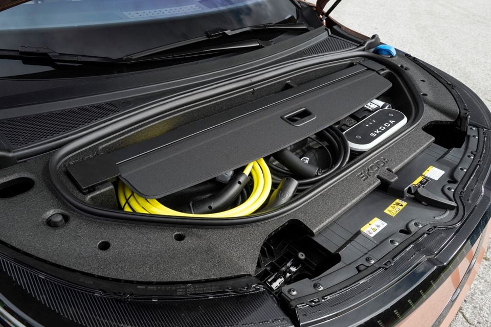 The frunk storage compartment of a Skoda Enyaq open to reveal a yellow EV charging cable and a Skoda-branded portable charger stored inside.