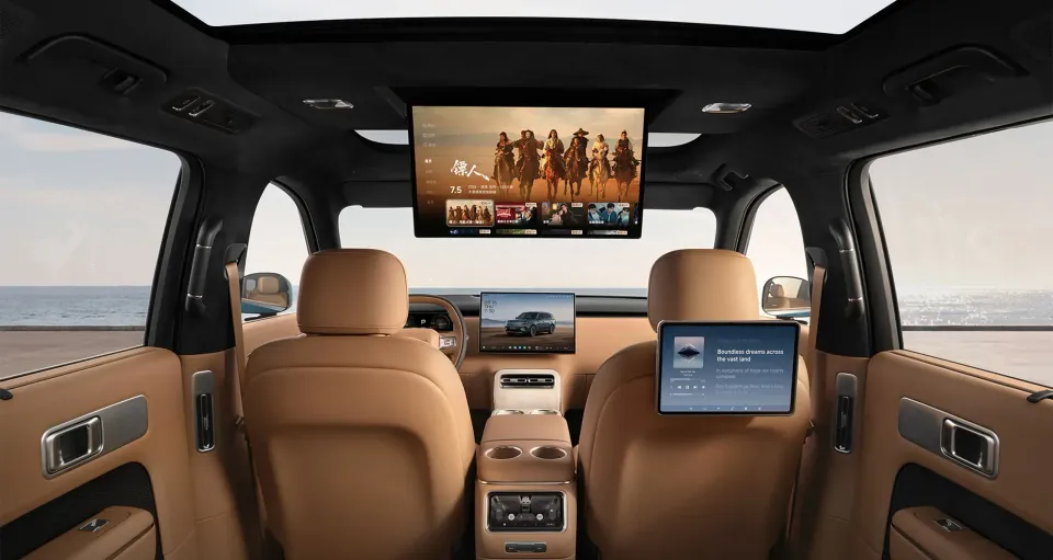 The rear passenger cabin of the Xiaomi YU7 SUV, featuring tan leather seats, a large roof-mounted entertainment screen, a central touchscreen, and a headrest-mounted tablet displaying media content