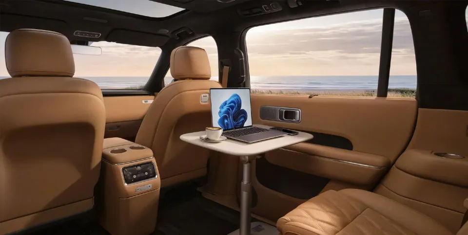 Tan leather rear cabin of the Xiaomi SkyNomad N90 SUV with a fold-out tray table holding a laptop and coffee cup, with a coastal sunset view through the windows