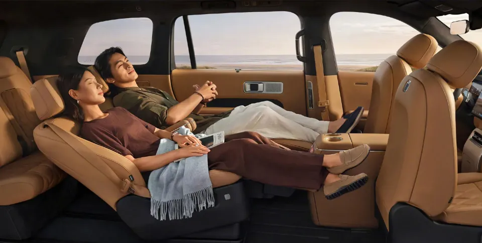 Two passengers recline in luxurious tan leather rear seats of a Xiaomi Skynomad N90 SUV, relaxing with a coastal view outside the windows