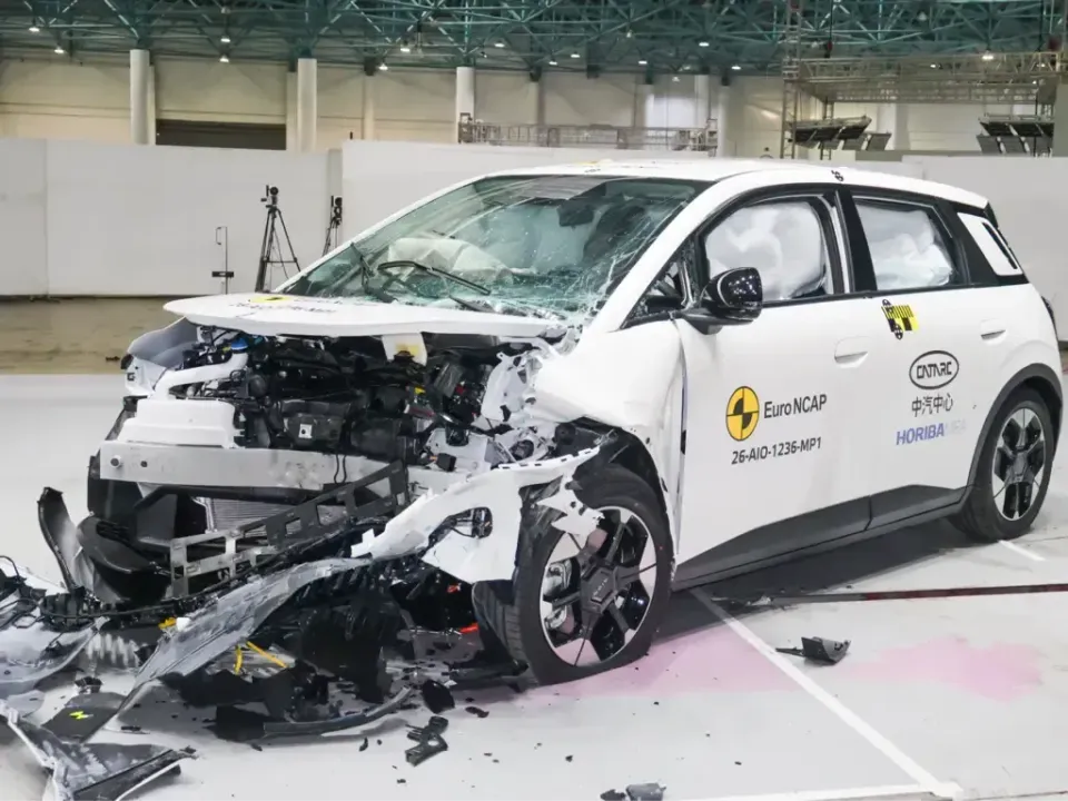 A white GAC Aion UT hatchback with a heavily damaged front end and deployed airbags after a Euro NCAP frontal crash test