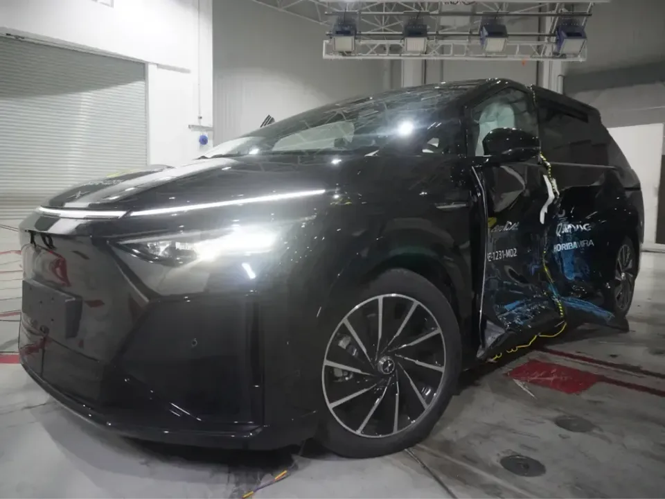 A black Xpeng X9 people mover with heavy side-impact damage to its driver's side doors after an ANCAP crash test, inside a testing facility