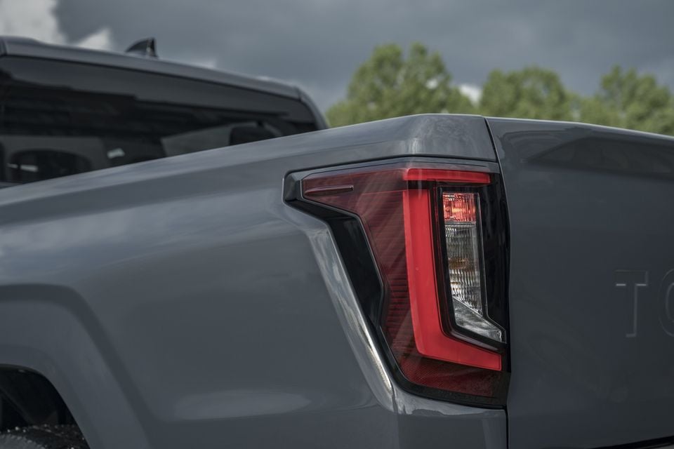 Close-up of the rear tail light on a grey 2026 Toyota HiLux BEV ute, showing the angular red LED light design on the tub corner