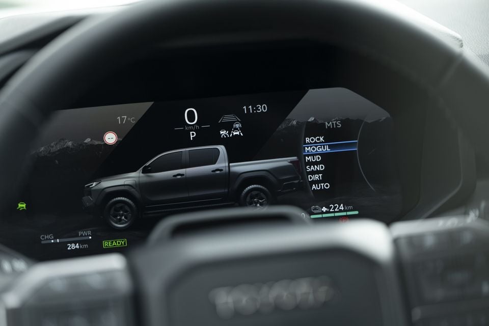 Digital instrument cluster of a 2026 Toyota HiLux BEV showing multi-terrain select modes including Rock, Mogul, Mud, Sand, Dirt and Auto, with a vehicle graphic and 284km range displayed