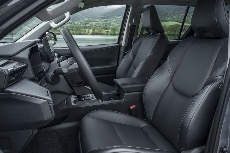 Interior view of a 2026 Toyota HiLux BEV showing black leather front seats, centre console, and steering wheel with a lakeside landscape visible through the windows.