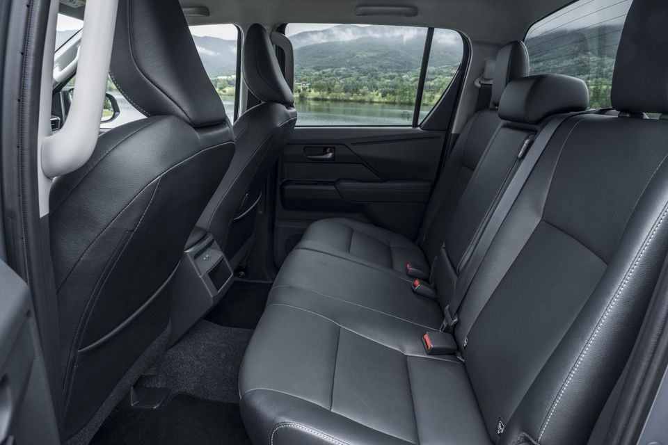 Rear interior of the 2026 Toyota HiLux BEV showing black leather rear bench seat with seatbelts, carpeted floor, and a scenic lake and mountain view through the windows