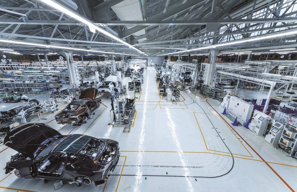 A wide-angle view of a large, modern car manufacturing facility with partially assembled vehicles on the production line.