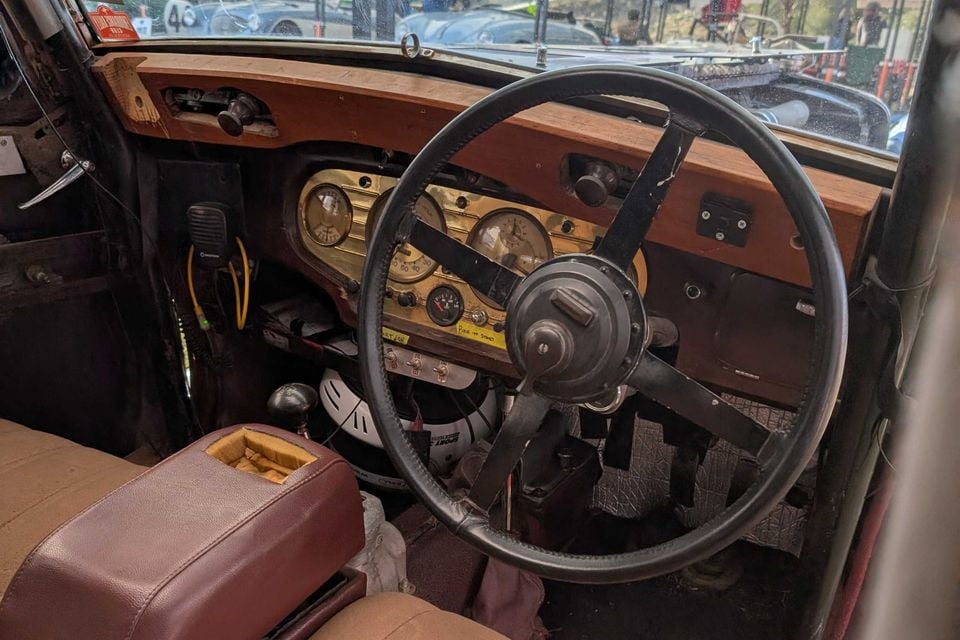 Wooden dashboard and large four-spoke steering wheel of a 1936 MG SA saloon, with brass-trimmed gauges and a burgundy centre armrest
