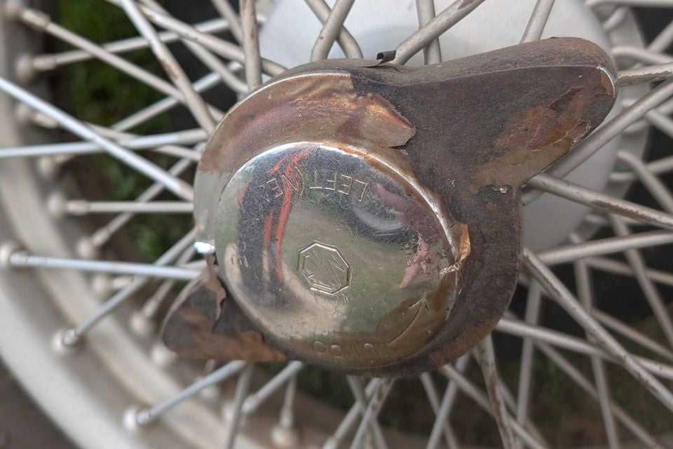 Close-up of the chrome knock-off wheel spinner on a 1936 MG SA saloon, stamped with the MG octagon badge and the word Left, mounted on a wire wheel