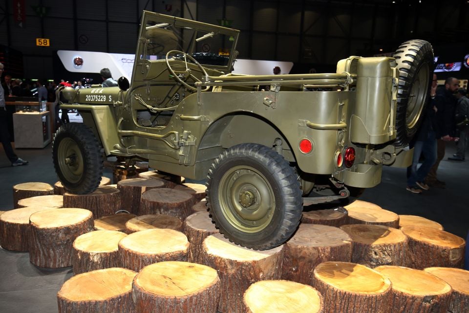 An olive green 1941 Willys Jeep military vehicle seen from the rear, displayed on tree stumps at a motor show