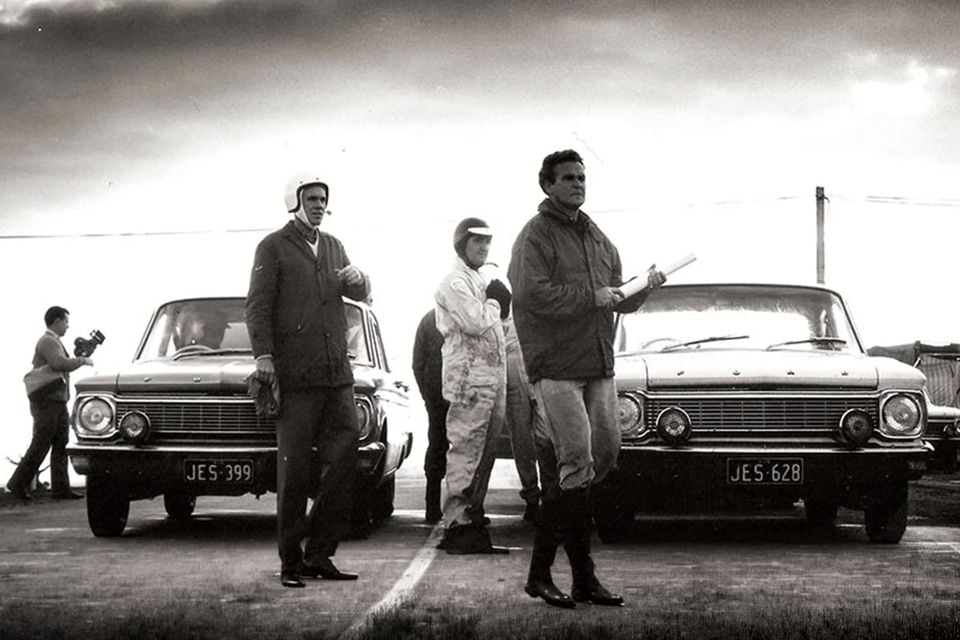 A black and white photo of two 1965 Ford Falcon XP sedans parked front-to-front with drivers and crew standing nearby during an endurance test at You Yangs