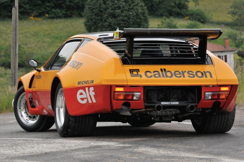 Um carro de rali Alpine A310 Grupo B 1977 laranja e vermelho com as cores Calberson e Elf, com uma grande asa traseira, visto da parte traseira