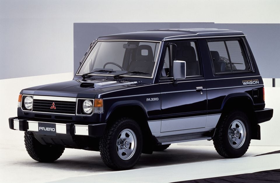A dark blue Mitsubishi Pajero short-wheelbase wagon seen from the front-side in a studio setting