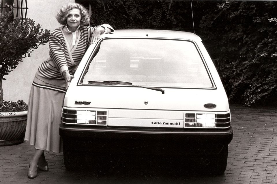 A woman poses beside a white 1985 Ford Laser Carla Zampatti hatchback, viewed from the rear.