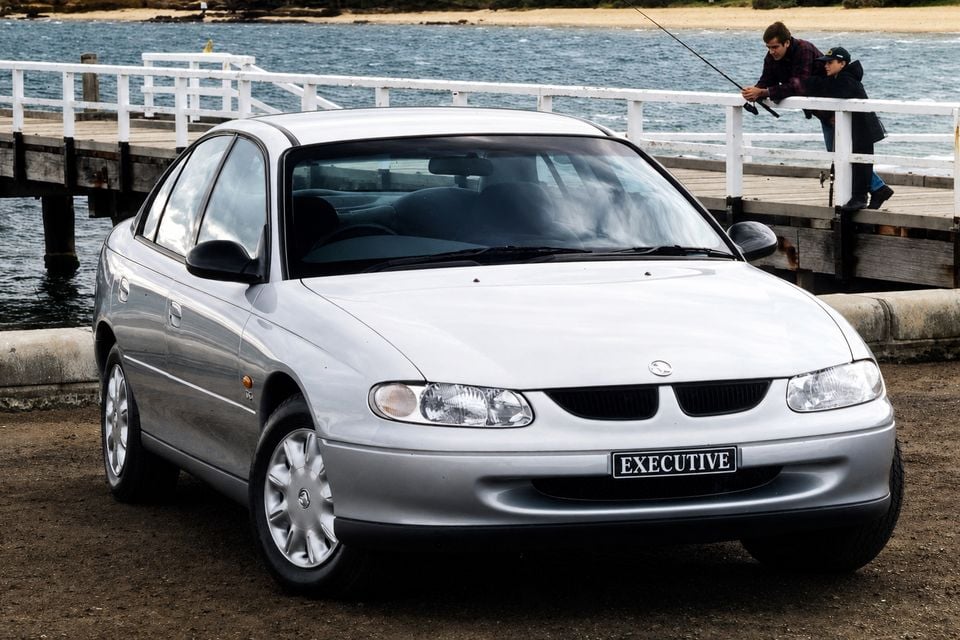 A silver Holden Commodore VT Executive sedan parked near a waterfront pier, seen from the front-side angle