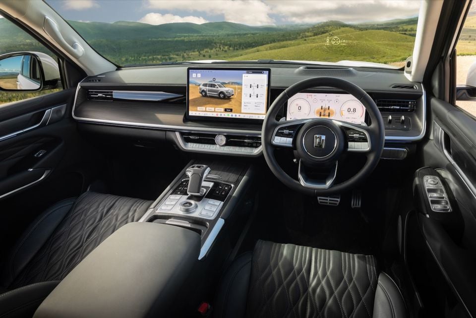 The dashboard and cockpit of a GWM Tank 500 SUV, showing the steering wheel, digital instrument cluster, infotainment screen and centre console with hills visible through the windscreen.
