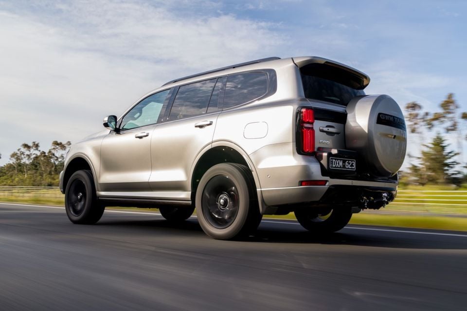 A silver 2026 GWM Tank 500 SUV with a rear-mounted spare wheel, photographed driving on a highway from the rear side angle