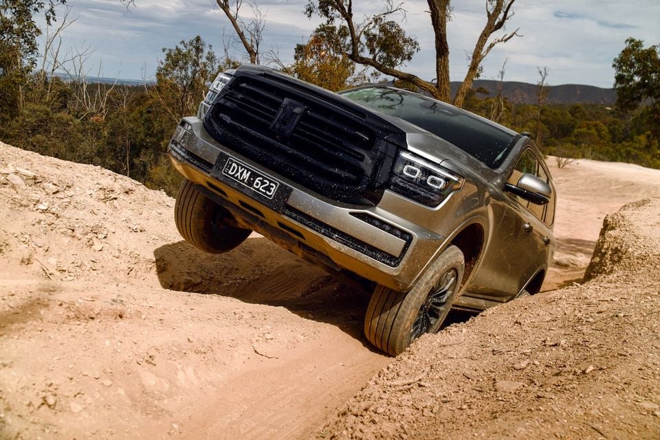 A GWM Tank 500 SUV navigates a rutted dirt track off-road, with its front wheels raised over a bump