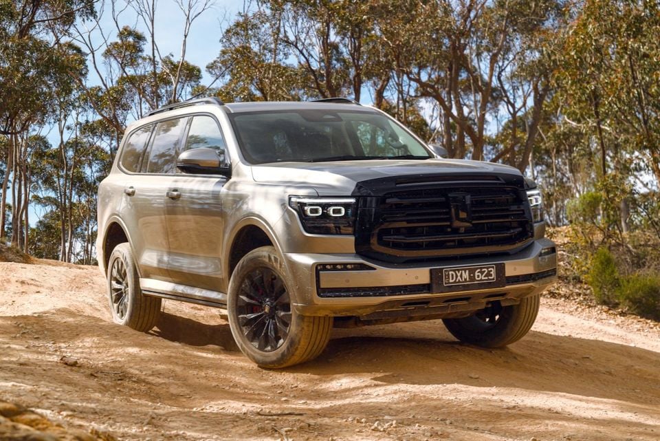 A silver 2026 GWM Tank 500 SUV parked on a dirt track surrounded by trees, seen from the front quarter.