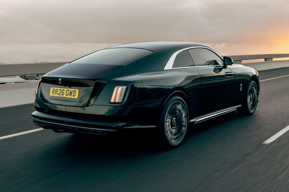 A dark green 2027 Rolls-Royce Spectre coupe driving on a motorway at dusk, seen from the rear