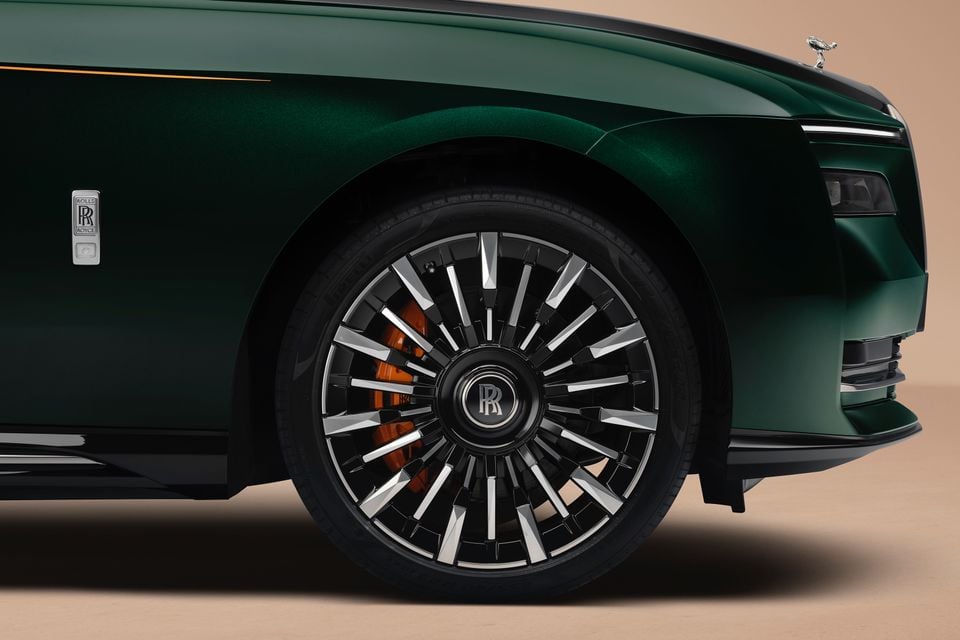 Close-up of the front wheel and orange brake caliper on a green 2027 Rolls-Royce Spectre, with its Spirit of Ecstasy mascot visible