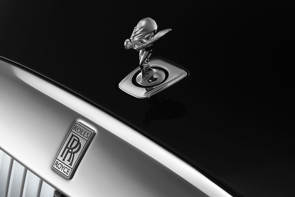 Close-up of the Spirit of Ecstasy mascot and Rolls-Royce badge on the black bonnet and silver grille surround of a 2027 Rolls-Royce Spectre