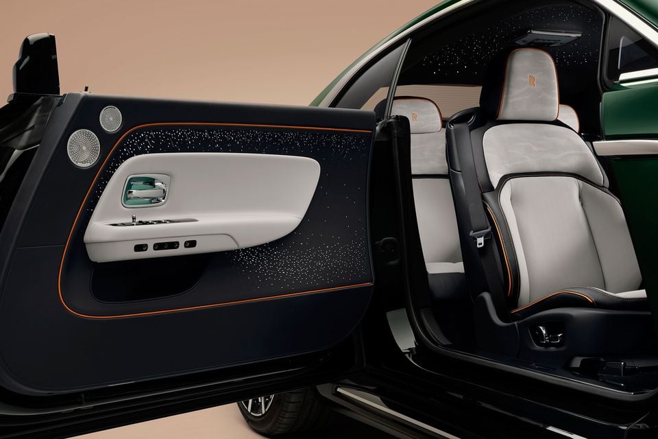 Open driver's door of a green 2027 Rolls-Royce Spectre showing a starlight door panel, speakers and grey and black front seats