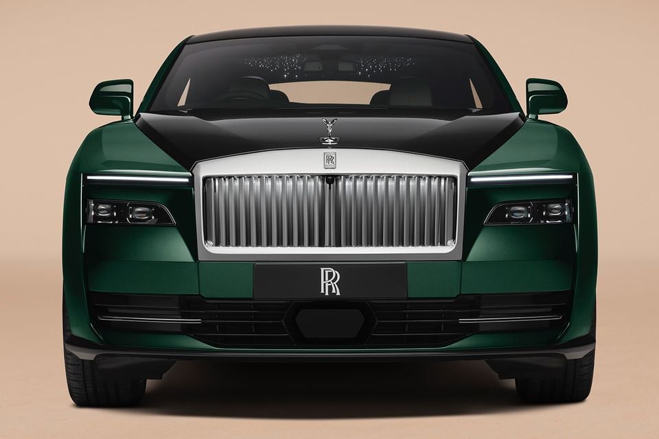 A green and black 2027 Rolls-Royce Spectre electric coupe seen from the front, showing its illuminated grille and Spirit of Ecstasy mascot