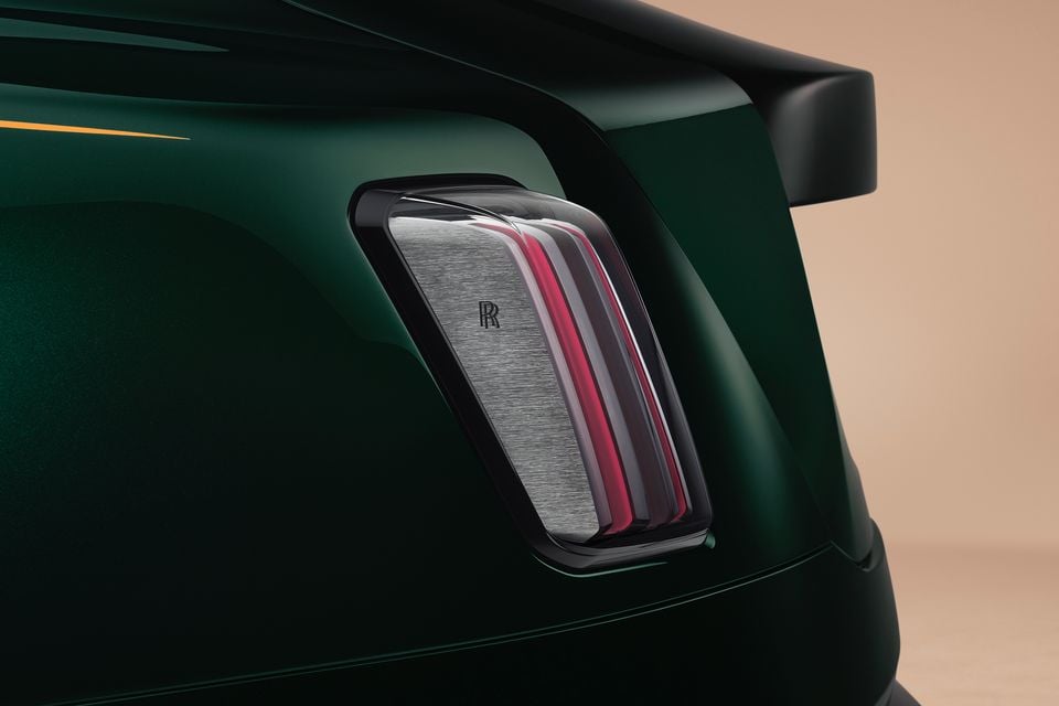 Close-up of the tail-light on a dark green 2027 Rolls-Royce Spectre, showing red light strips and a brushed-metal panel with the RR logo