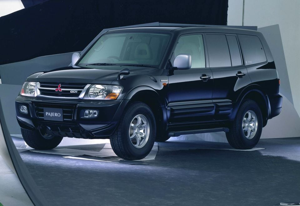 A black Mitsubishi Pajero GDI large SUV photographed in a studio setting, seen from the front-left angle