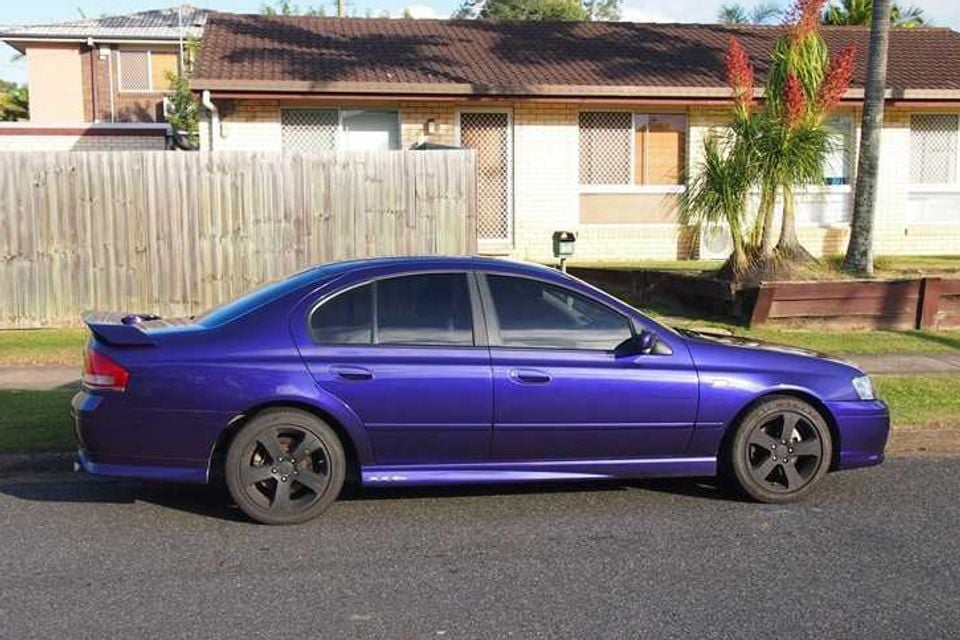 A purple Ford Falcon XR6 sedan with a rear spoiler parked on a residential street, seen from the side.