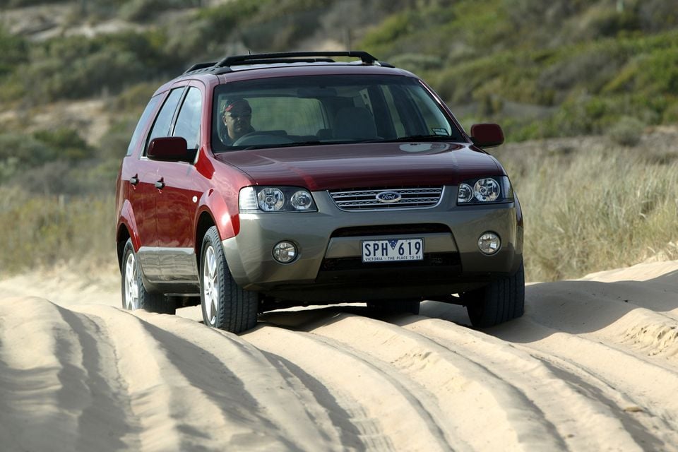 A maroon and grey 2004 Ford Territory SUV driving over sand dunes, seen from the front quarter angle.
