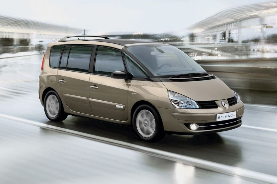 Uma minivan Renault Espace 2006 bege dirigindo em uma estrada molhada, vista do ângulo frontal.
