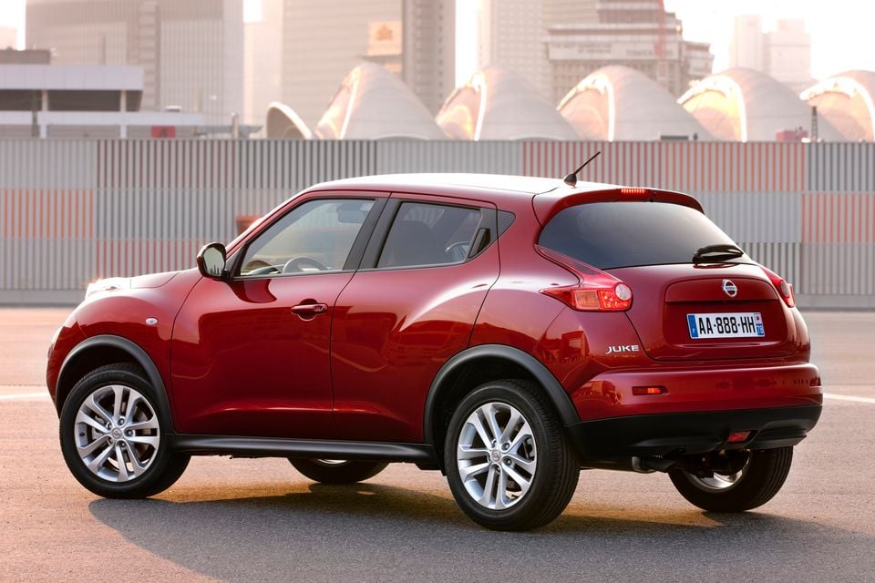 A red Nissan Juke small SUV seen from the rear three-quarter angle in an urban setting