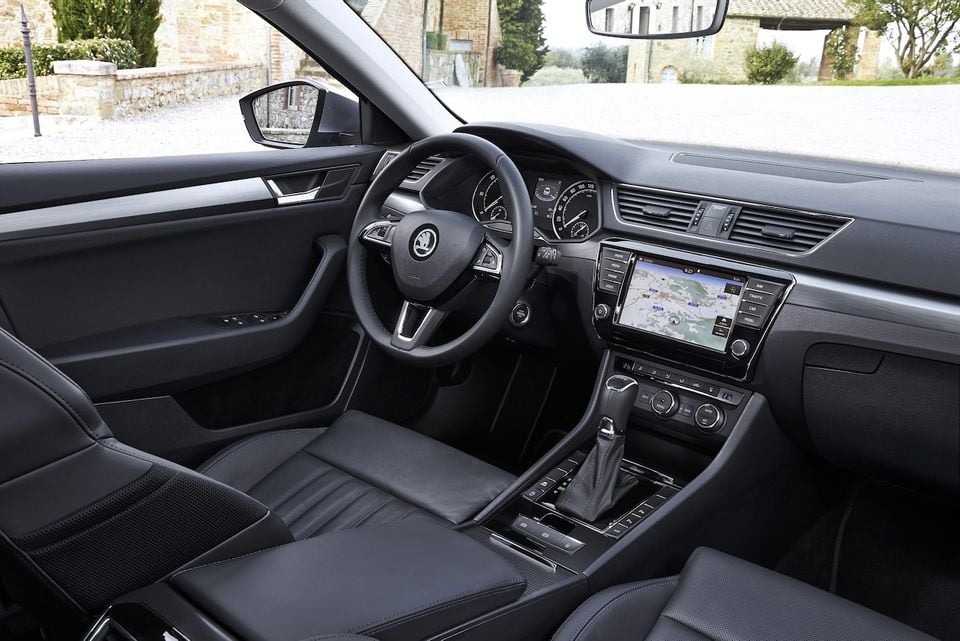 Interior of a Skoda Superb showing the dashboard, steering wheel, centre console, and touchscreen infotainment system with navigation displayed