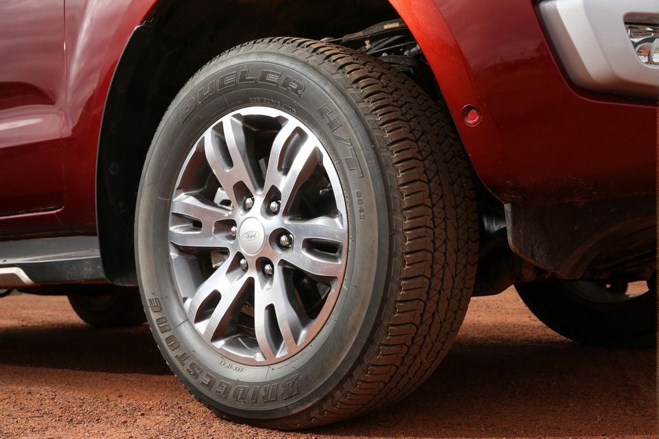 Close-up of a Bridgestone Dueler H/T tyre on a silver alloy wheel with a Ford centre cap, fitted to a red Ford Everest on red dirt ground