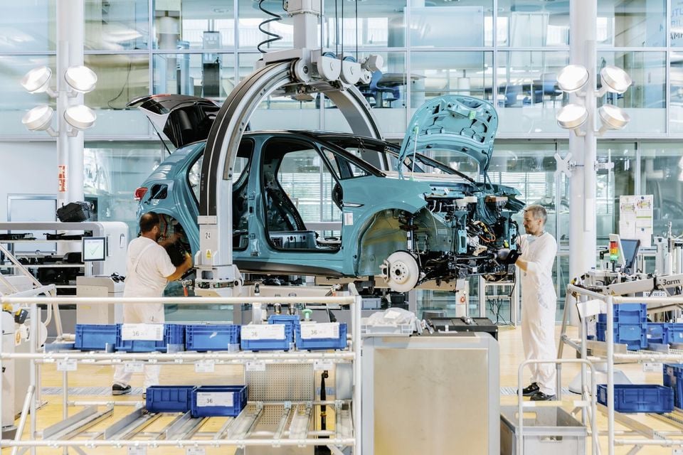 Two workers in white overalls assembling a light blue Volkswagen ID.3 body shell suspended on a production line inside the Glaeserne Manufaktur (Glass Factory) in Dresden, Germany.