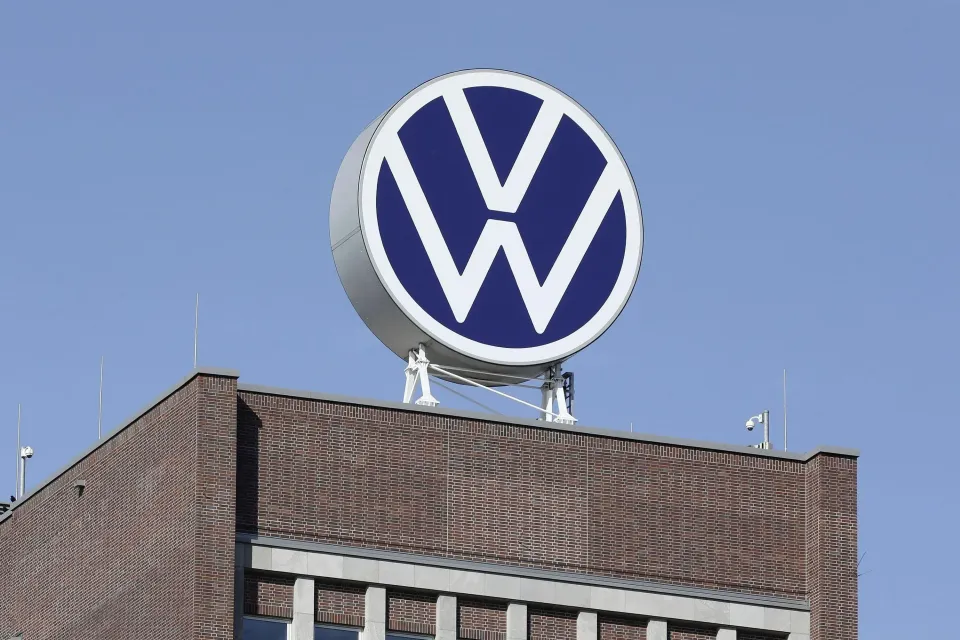 The Volkswagen logo on a large circular sign mounted on top of a brick building against a clear blue sky.