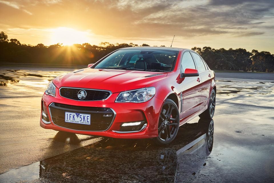 A red Holden Commodore SS V Redline VF II sedan photographed from the front-side angle at sunset on a wet open surface in Victoria, Australia.