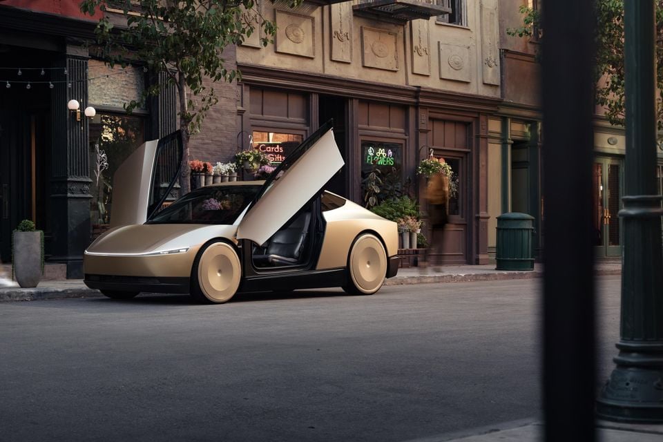 A gold Tesla Cybercab concept car with scissor doors open, parked on a city street in front of a flower shop
