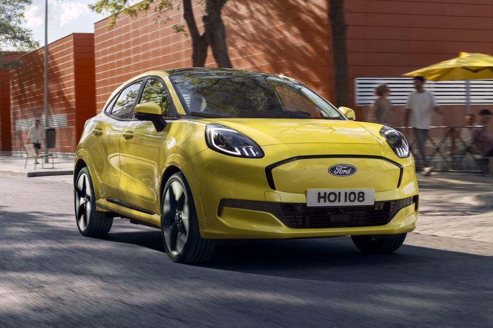 A yellow Ford Puma Gen-E small SUV driving on a city street, seen from the front-side angle