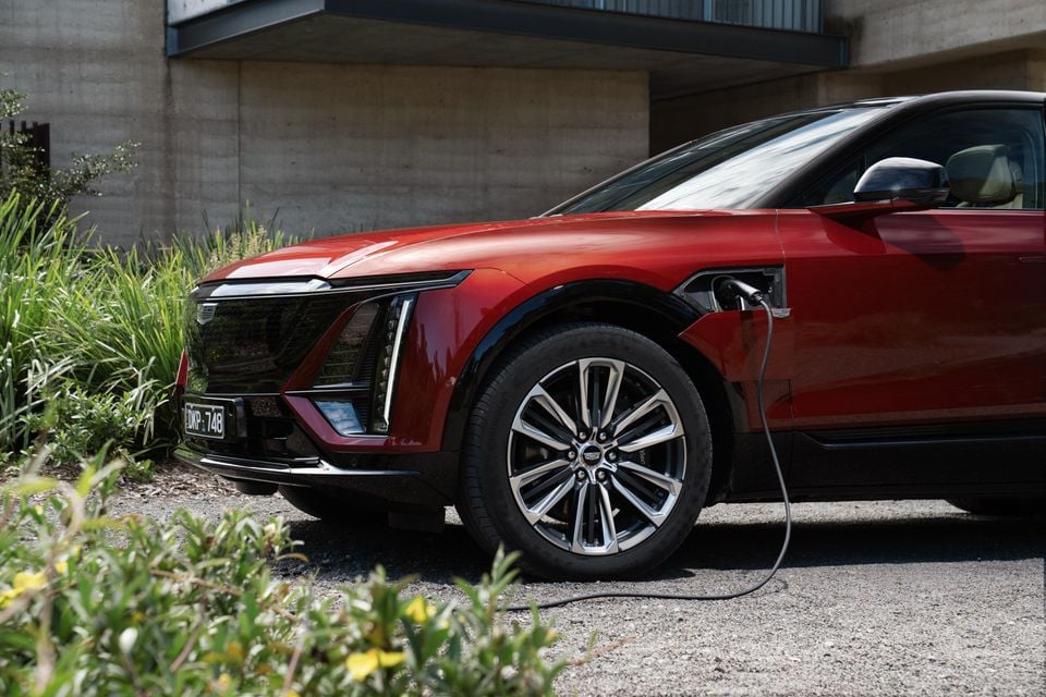 A red 2025 Cadillac Lyriq electric SUV plugged in and charging, seen from the front side