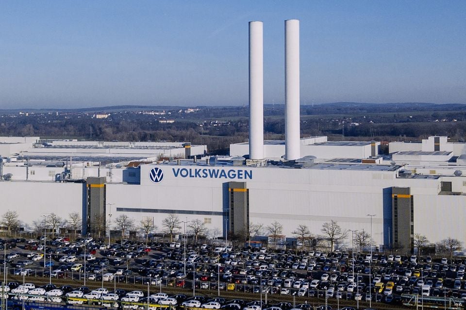 Aerial view of the Volkswagen Zwickau manufacturing plant with hundreds of cars parked in the foreground and two tall white chimneys rising above the factory building