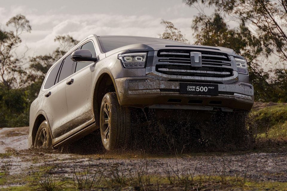 A GWM Tank 500 PHEV large SUV driving through mud on an off-road track, seen from the front-side angle