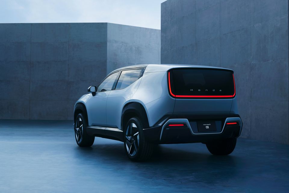 A silver Honda 0 Series Alpha concept SUV shown from the rear quarter angle with an illuminated red taillight bar, parked in a concrete courtyard.