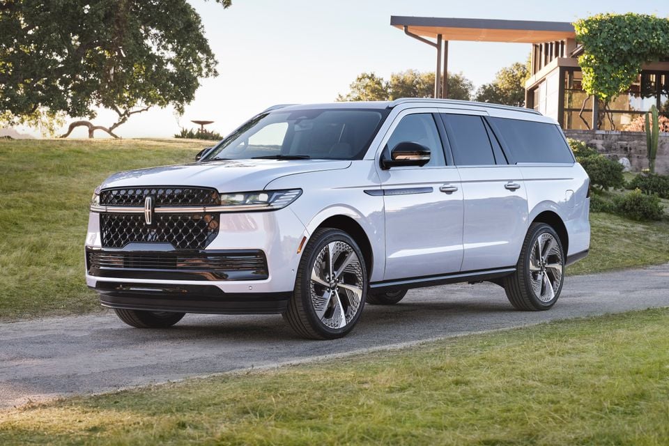 A white 2025 Lincoln Navigator L large SUV seen from the front-side angle on a gravel driveway beside a modern home