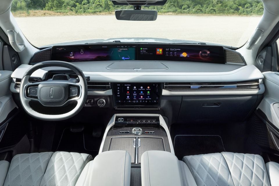 Interior dashboard view of a 2025 Lincoln Navigator L Black Label, featuring a wide panoramic display screen, central touchscreen infotainment system, quilted light grey leather seats and centre console