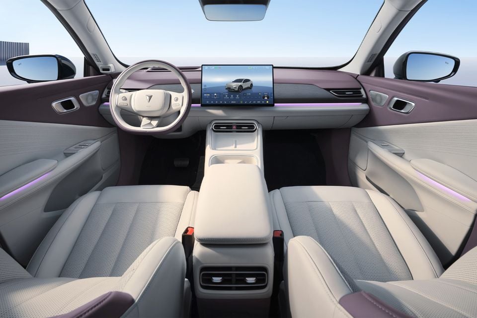 Interior of the 2025 Deepal S05 showing the dashboard, large central touchscreen infotainment display, steering wheel, front seats, and ambient lighting with a two-tone cream and mauve colour scheme